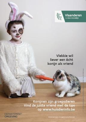 Kind verkleed als konijn geeft een wortel aan een konijn dat wegkijkt. De tekst meldt: Vlekkie wil liever een echt konijn als vriend.